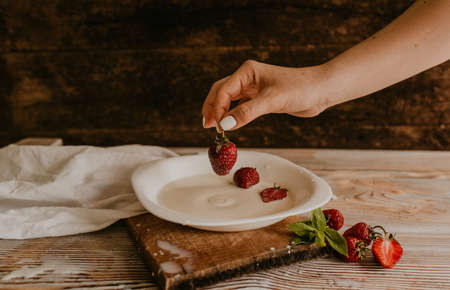scattered juicy fresh red strawberries on the table with vintage plank. mint leaf. drops and splashes of spilled milk. vegetable cutting board. High quality photoの写真素材