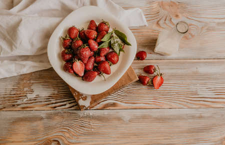 scattered juicy fresh red strawberries on the table with vintage plank. mint leaf. drops and splashes of spilled milk. vegetable cutting board. High quality photoの写真素材