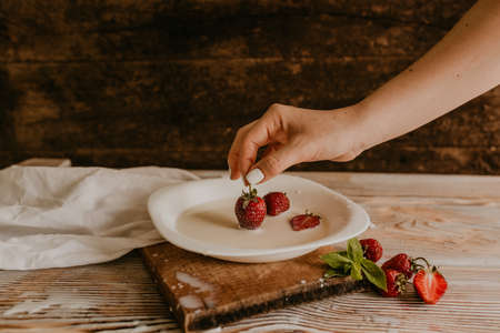 scattered juicy fresh red strawberries on the table with vintage plank. mint leaf. drops and splashes of spilled milk. vegetable cutting board. High quality photoの写真素材