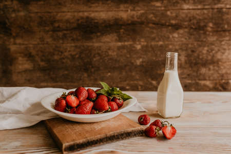 scattered juicy fresh red strawberries on the table with vintage plank. mint leaf. drops and splashes of spilled milk. vegetable cutting board. High quality photoの写真素材