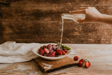 scattered juicy fresh red strawberries on the table with vintage plank. mint leaf. drops and splashes of spilled milk. vegetable cutting board. High quality photoの写真素材
