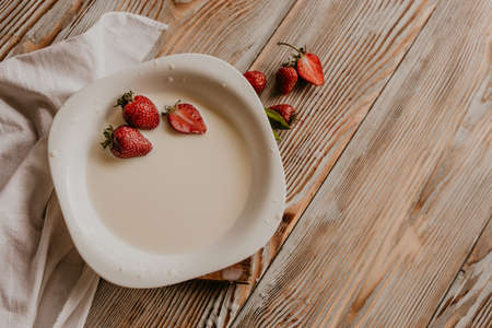 scattered juicy fresh red strawberries on the table with vintage plank. mint leaf. drops and splashes of spilled milk. vegetable cutting board. High quality photoの写真素材