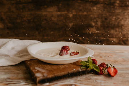scattered juicy fresh red strawberries on the table with vintage plank. mint leaf. drops and splashes of spilled milk. vegetable cutting board. High quality photoの写真素材