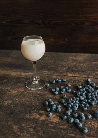A transparent glass with milk. Blue fresh blueberries are scattered on an old brown wooden cracked table.の写真素材