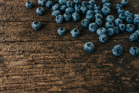 Blue fresh blueberries are scattered on an old brown wooden cracked table.