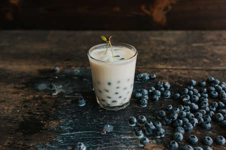 Red cherry hangs on a glass, everything is covered with sesame seeds on top, milk is spilled on the table. Blueberries float in a transparent glass with milk. Blue fresh blueberries are scatteredの写真素材