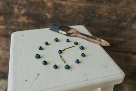 Fresh blue matte round blueberries. on wooden white chairs lie berries folded in a circle in the shape of a clock. blue paint brushの写真素材
