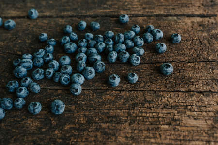 Blue fresh blueberries are scattered on an old brown wooden cracked table.の写真素材