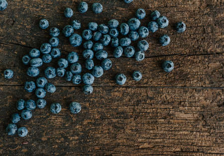Blue fresh blueberries are scattered on an old brown wooden cracked table.の写真素材