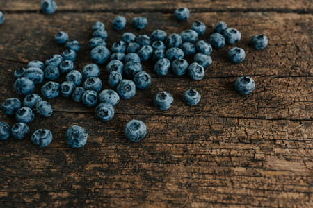 Blue fresh blueberries are scattered on an old brown wooden cracked table.の写真素材