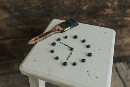 Fresh blue matte round blueberries. on wooden white chairs lie berries folded in a circle in the shape of a clock. blue paint brushの写真素材