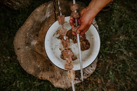 Male hands are holding metal skewers and putting raw marinated pork veal blood chicken meat over a bowl.の写真素材