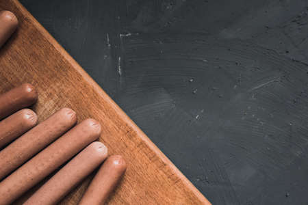 Boiled fried sausages sausages lie on a wooden kitchen board scratched against a dark concrete background.の写真素材