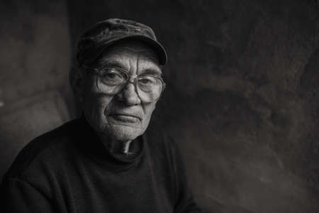 Pensive old man in glasses with gray hair looks away. wrinkles. wisdom. against a dark gray texture wall. bald head. in a knitted sweater. Portrait.の写真素材