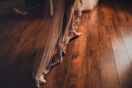 The brides legs in white stockings walk along the brown wooden parquet floor, there is a long lace veil in the back. dark backgroundの写真素材