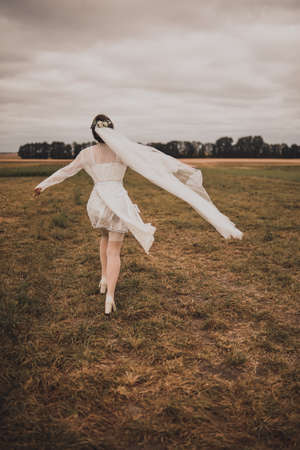 Wedding decorations jewelry on head. Beautiful green wreath with flower holds a veil. young slim beautiful woman high Greek hairstyle in White Silk in a bathrobe. green natural background.Running awayの写真素材