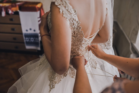 The back of the bride in a wedding dress. Moms and womans hands help fasten the clasps at the back.