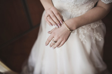 The female hands of the fair-skinned bride lie on the white wedding dress. A ring on the hand of a young girl.の写真素材