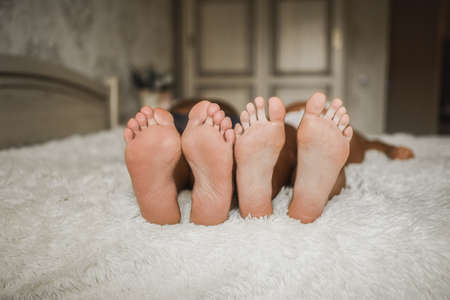 Adult man and a woman with bare feet are lying on the bed. Clean soles of the feet of European white people. Bright cozy small room on the background.の写真素材