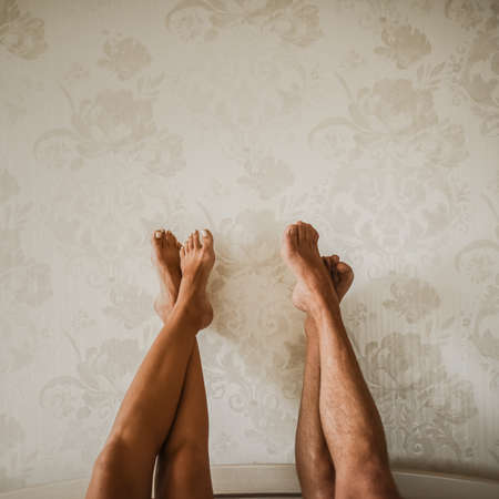 Tanned male nude and female legs crossed raised up against the wall.の写真素材