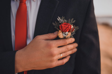 A man with a wedding ring on his finger holds a wedding boutonniere on his jacket. hands of the...