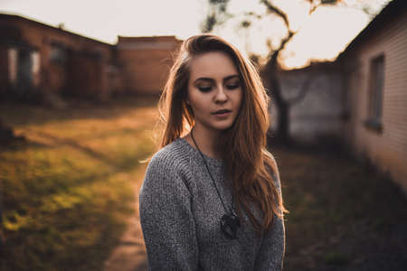 beautiful young blonde model girl. gray knitted sweater. wooden pendant on the neck in the form of a horse. On the Sunset. Portrait. best retouchの写真素材