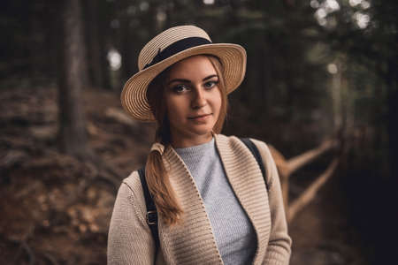 Slavic tanned fair-haired young girl with a boater hat on nature. Traveler tourist in a dark forest. constant tone of clothes. dark brown backgroundの写真素材
