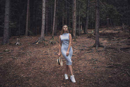 Slavic tanned fair-haired young girl with a boater hat on nature. Traveler tourist in a dark forest. constant tone of clothes. dark brown backgroundの写真素材