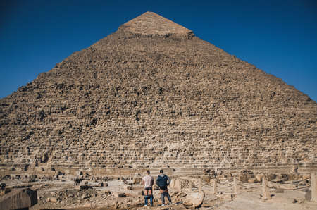 Two men stand in front of the old pyramid with their pants down.の写真素材