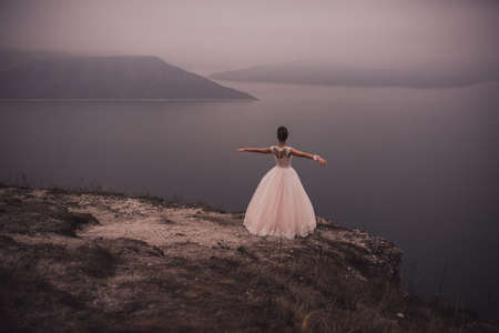 young slim beautiful woman Bride with a high Greek hairstyle and embellishment and in a White green puffy wedding dress stands on a cliff on top of a mountain. looks into the distance at sea the mountの写真素材