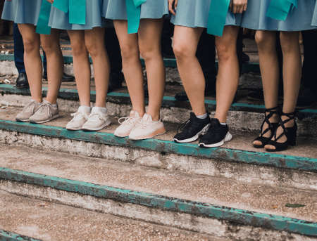 thin girls legs in blue short skirts shod in different shoes stand on the steps together. School class at graduation.の写真素材