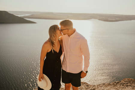 A man and a woman in love walk on a mountain above a large lake by the sea at sunset. A couple of fair-haired fair-skinned people in love are resting in nature in a fieldの写真素材