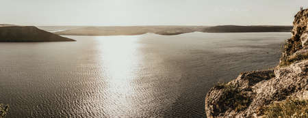 Panoramic view A couple of people in love, a man and a woman, stand on the Big Mountain above the cliff over the sea with islands at sunset. View from a drone on a huge stone rock.の写真素材