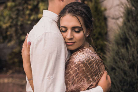 Young couple of lovers man and woman in festive fashionable clothes are hugging. Light casual hairstyle for women with a perm. Summer nature outside background.の写真素材