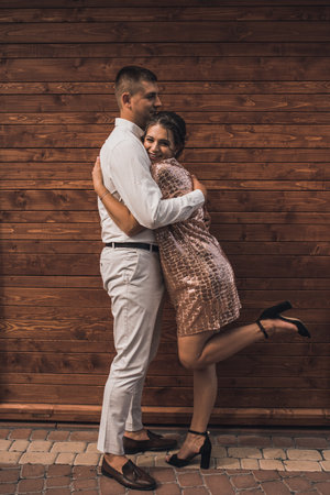 Young couple of lovers man and woman in festive fashionable clothes are hugging. Light casual hairstyle for women with a perm. wood brown plank backgroundの写真素材
