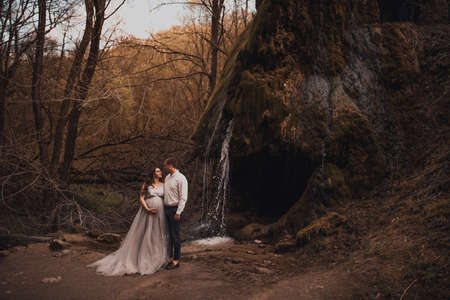 Family couple a man with a pregnant woman with a big belly in nature on the background of a waterfall.の写真素材