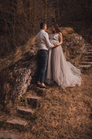 married couple a man with a pregnant woman with a big belly in nature near the mountain are walking on stone stepsの写真素材