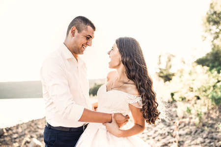 bride and groom in wedding dress happy and laughing run together against rays of setting sun in summer Bakota, Ukraineの写真素材