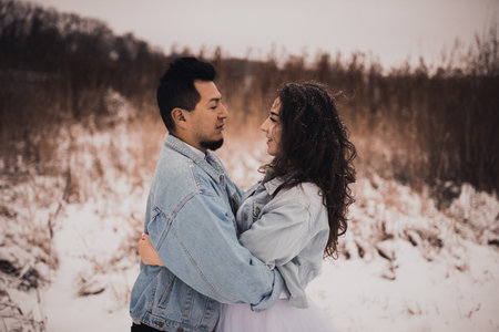 Mexican Hispanic man in denim jacket oversized and woman are kissing hugging laughing. groom and bride wedding love couple in winter in snow. fashionable stylish party wedding wearの写真素材