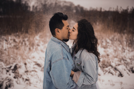 Mexican Hispanic man in denim jacket oversized and woman are kissing hugging laughing. groom and bride wedding love couple in winter in snow. fashionable stylish party weddingの写真素材