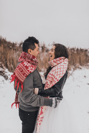 young man and woman running lying in the snow laughing fooling around having fun playing snowballs.bride and groom in love couple in knitted scarf and mittens in winter and snowflakes. mexican peopleの写真素材