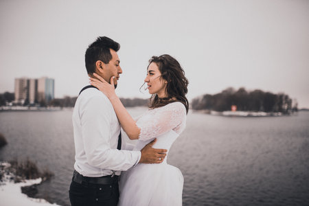 Mexican Hispanic man in suspenders and woman are kissing hugging laughing. groom and bride wedding love couple in winter in snow. fashionable stylish party wedding wearの写真素材