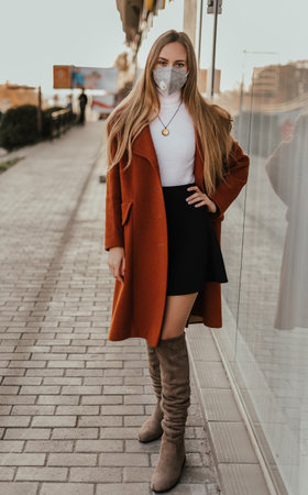 young ukrainian blonde woman in protective medical mask kn95 respirator on street against background of shop windows. coronavirus infection. accessory covid-19の写真素材