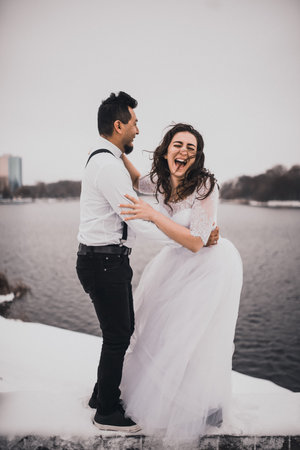 Mexican Hispanic man in suspenders and woman are kissing hugging laughing. groom and bride wedding love couple in winter in snow. fashionable stylish party wedding wear 2021の写真素材
