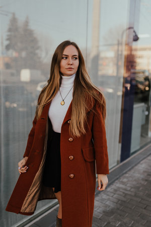 young blonde woman in autumn clothes walks on street background shop windows. Street style Fashion 2021 Winter Spring Terracotta Coat Woolen Cashmere Suede Over Knee Boots White Golfの写真素材