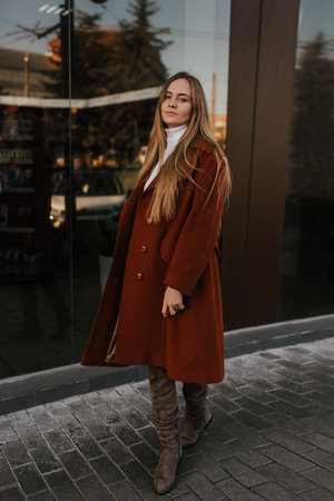 young blonde woman in autumn clothes walks on street background shop windows. Street style Fashion 2021 Winter Spring Terracotta Coat Woolen Cashmere Suede Over Knee Boots White Golfの写真素材