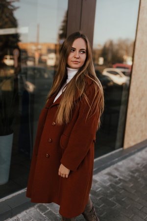 young blonde woman in autumn clothes walks on street background shop windows. Street style Fashion 2021 Winter Spring Terracotta Coat Woolen Cashmere Suede Over Knee Boots White Golfの写真素材