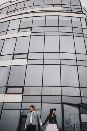 Mexican Hispanic man and woman in hat are kissing hugging laughing walking. groom bride wedding love couple in winter in snow on background of shop windows.fashionable stylish party wedding wearの写真素材