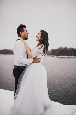 Mexican Hispanic man in suspenders and woman are kissing hugging laughing. groom and bride wedding love couple in winter in snow. fashionable stylish party wedding wear 2021の写真素材