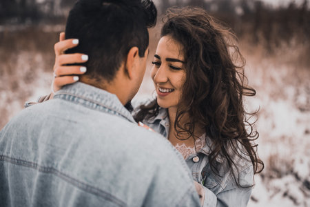Mexican Hispanic man in denim jacket oversized and woman are kissing hugging laughing. groom and bride wedding love couple in winter in snow. fashionable stylish party wedding wear 2021の写真素材